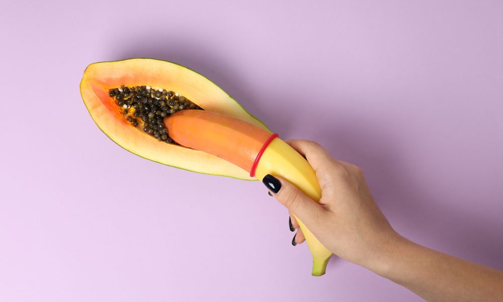 Woman's hand holding banana over papaya
